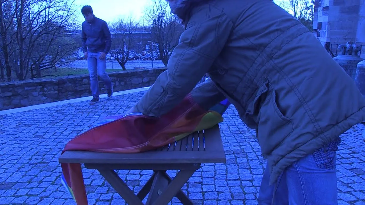 Person poliert braune Lederschuhe auf einem Hocker in einer abendlichen Parkanlage mit blauer Beleuchtung.