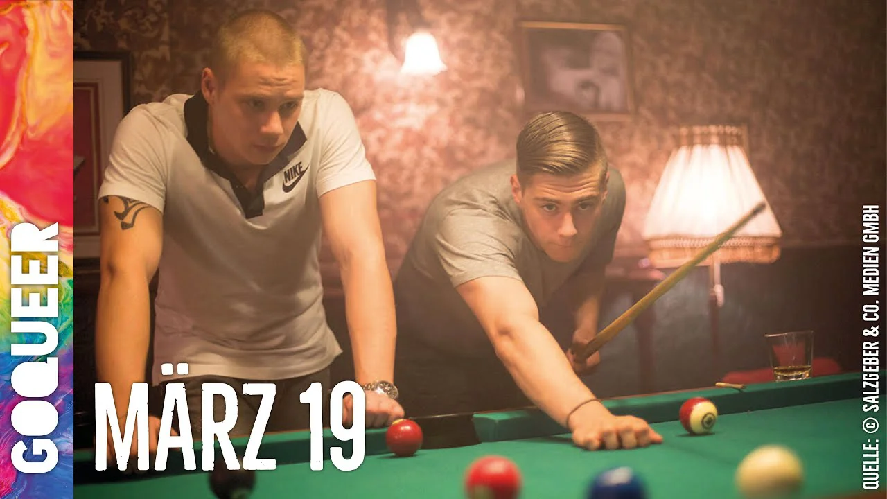 Zwei junge Männer spielen konzentriert Billard an einem grünen Tisch in gedämpftem Licht.