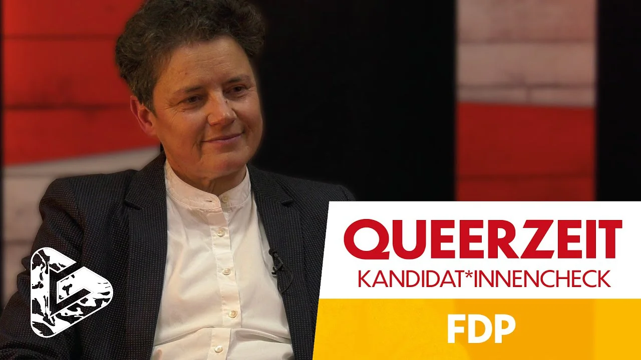 Person in dunklem Blazer und weißer Bluse vor rotem Hintergrund, rechts Logo "QUEERZEIT KANDIDAT*INNENCHECK FDP".