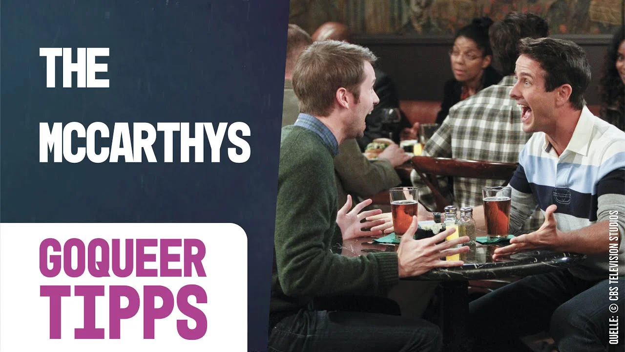 Zwei Männer sitzen an einem Tisch und unterhalten sich angeregt beim Essen, während andere Personen im Hintergrund sind.