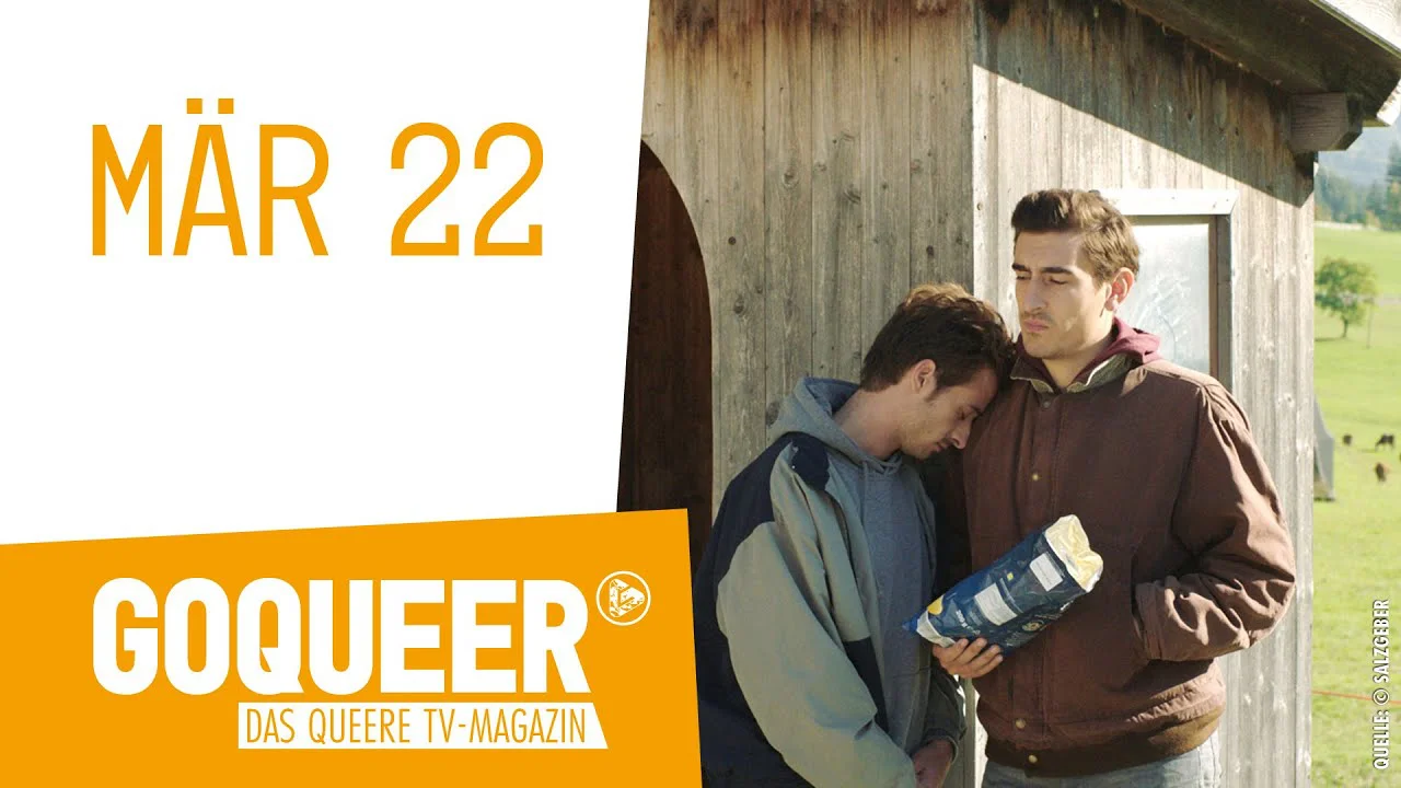 Zwei Männer stehen vor einer Holzhütte, einer lehnt sich an den anderen und hält eine Flasche.