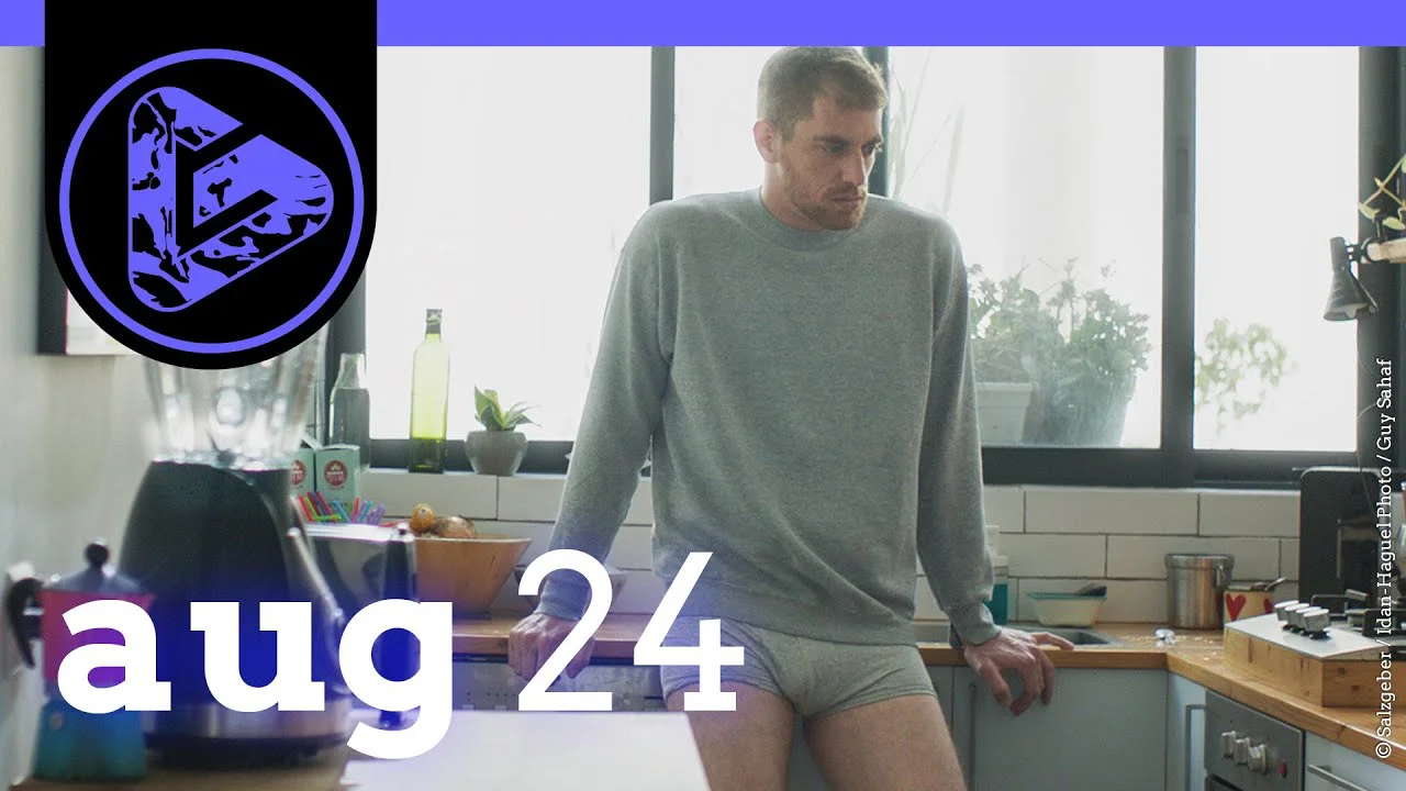 Mann in grauem Pullover und Shorts steht in einer Küche, Datum "aug 24" eingeblendet.