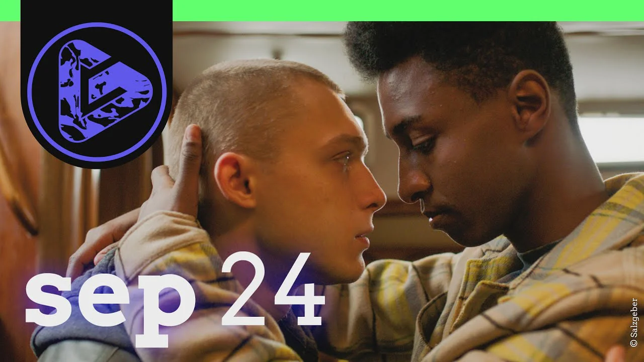 Zwei Männer in Militärjacken blicken sich nah gegenüber an, dazu Text "sep 24" und ein Logo.
